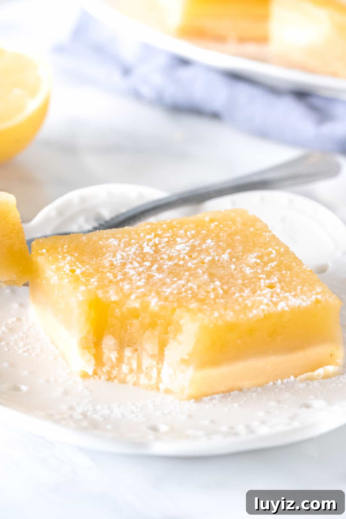 Tangy Lemon Bars Recipe with Buttery Shortbread Crust 6 Lemon slice on a plate with a bite taken out of it.