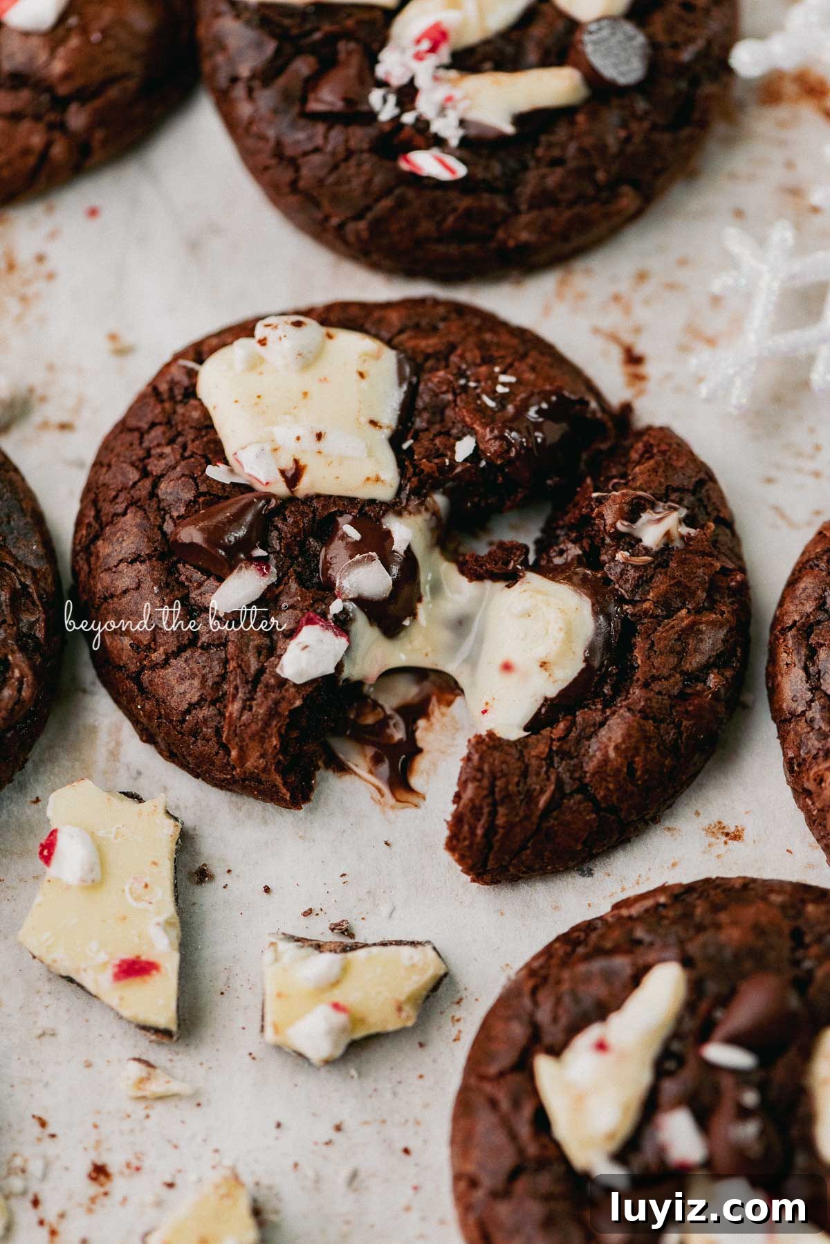 Peppermint Bark Brownie Crinkle Cookies Recipe for the Holidays 3 A split peppermint bark brownie crinkle cookie on a parchment paper lined baking sheet | © Beyond the Buter®