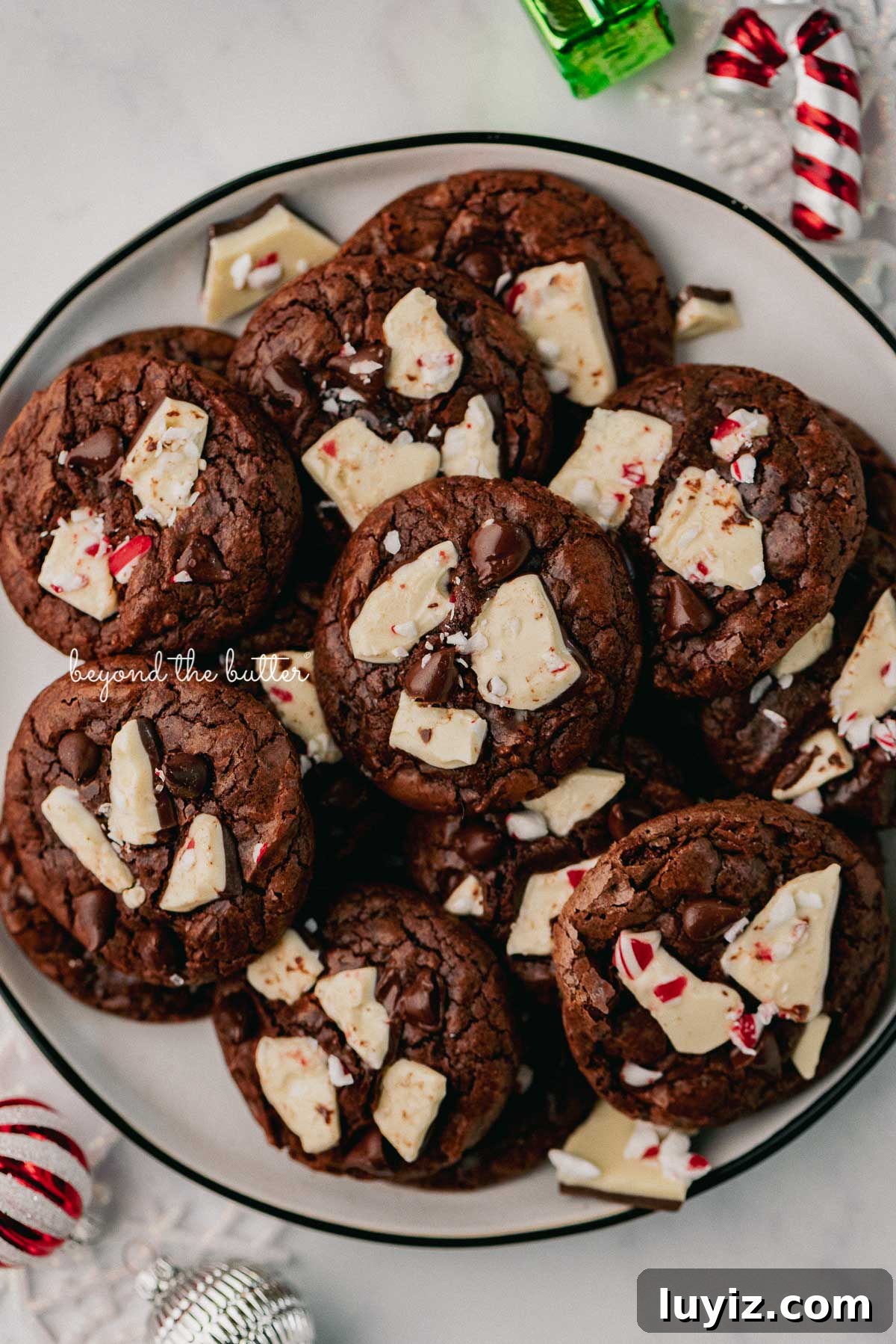 Peppermint Bark Brownie Crinkle Cookies Recipe for the Holidays 5 Plate full of peppermint bark brownie crinkle cookies with ornaments around the plate | © Beyond the Butter®