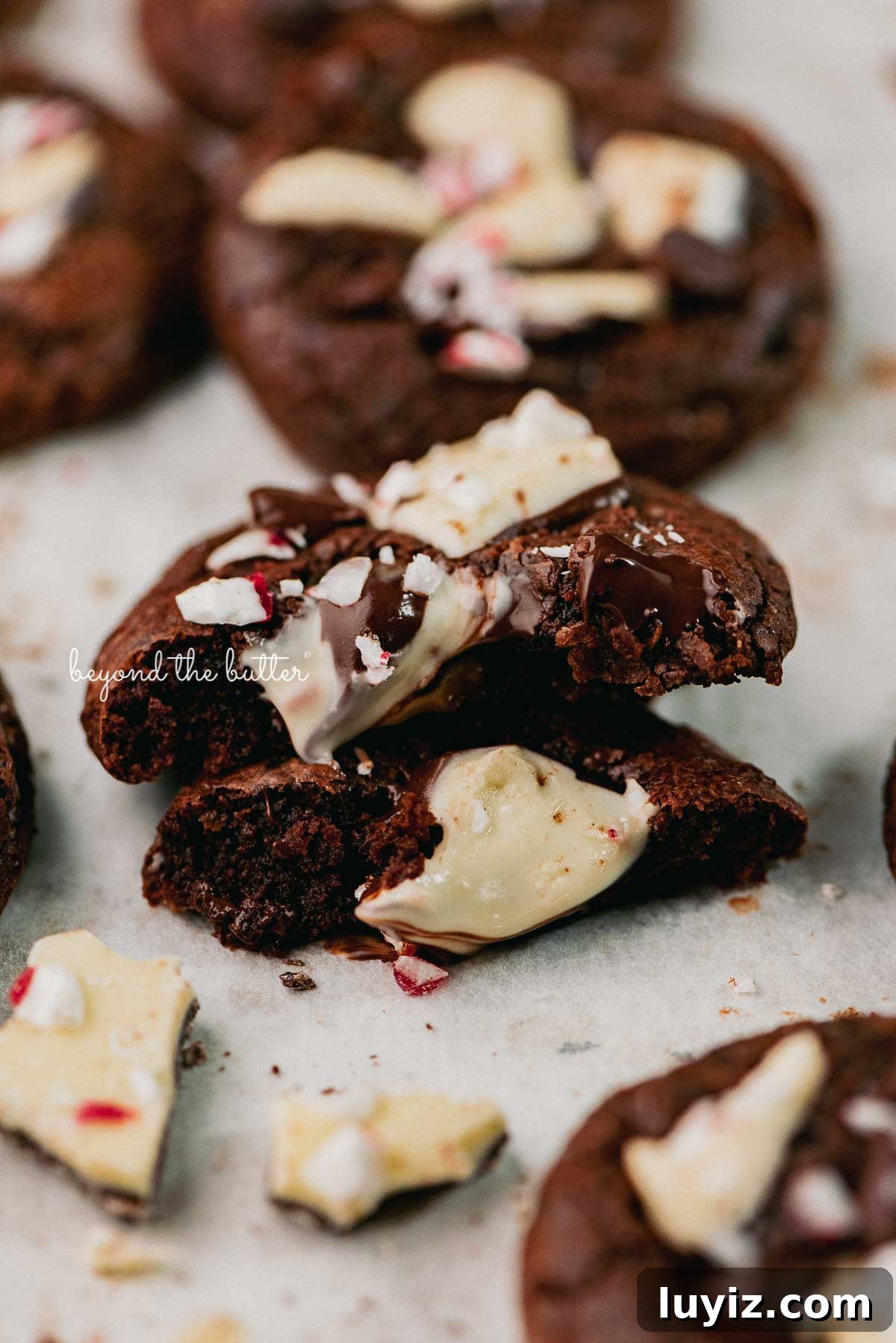 Peppermint Bark Brownie Crinkle Cookies Recipe for the Holidays 6 A split peppermint bark brownie crinkle cookie on a parchment paper lined baking sheet | © Beyond the Buter®