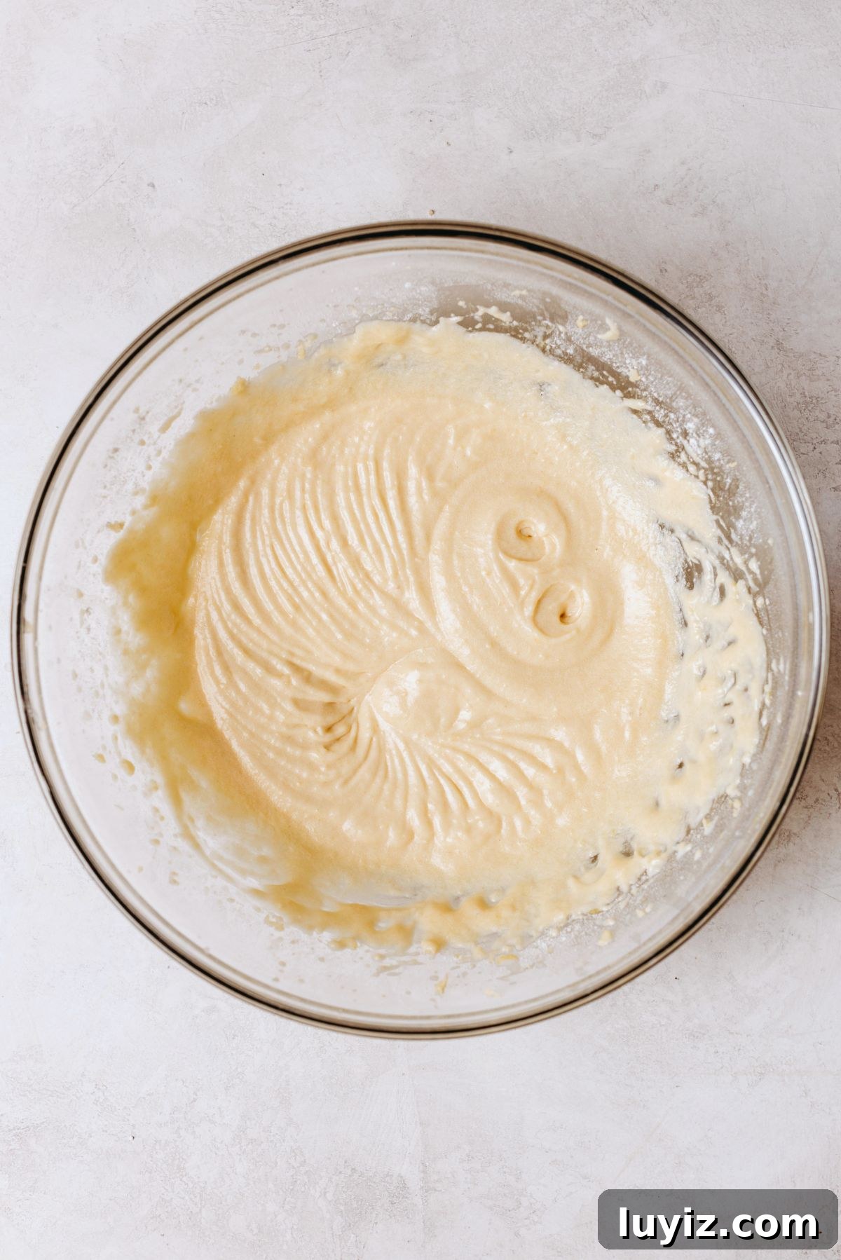 Chocolate Chip Cookie Dough Cupcakes Recipe with Gooey Centers 11 Added milk and vanilla extract into vanilla cupcake batter in a large glass mixing bowl on a white marbled background.