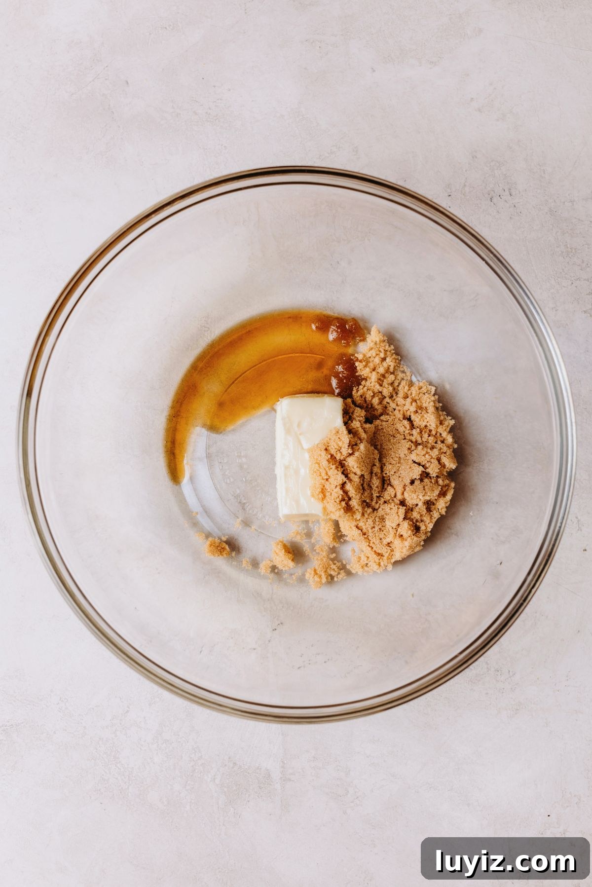 Chocolate Chip Cookie Dough Cupcakes Recipe with Gooey Centers 14 Light brown sugar, unsalted butter, and vanilla extract in a large glass mixing bowl on a white marbled background.