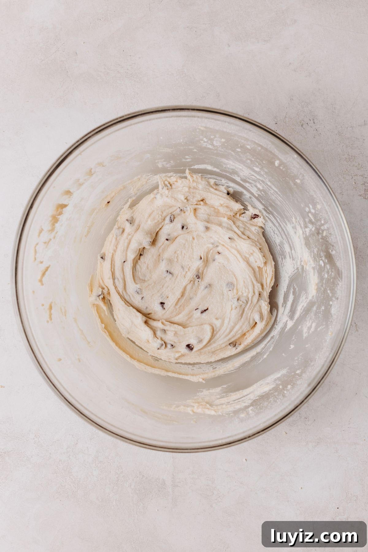 Chocolate Chip Cookie Dough Cupcakes Recipe with Gooey Centers 17 Mini semi sweet chocolate chips folded into cookie dough buttercream frosting in a large glass mixing bowl.