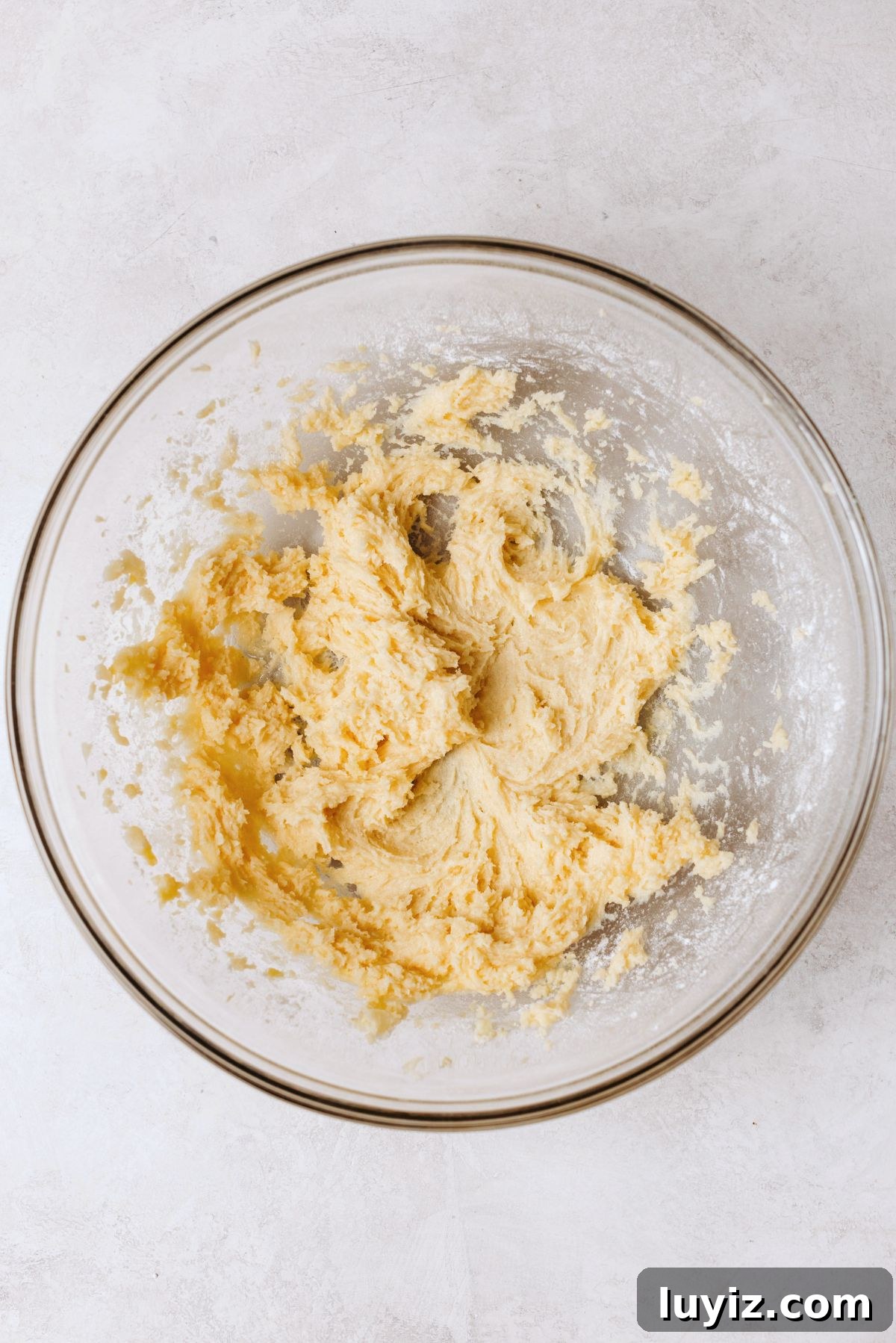 Chocolate Chip Cookie Dough Cupcakes Recipe with Gooey Centers 10 Mixing vanilla cupcake batter in a large glass mixing bowl on a white marbled background.