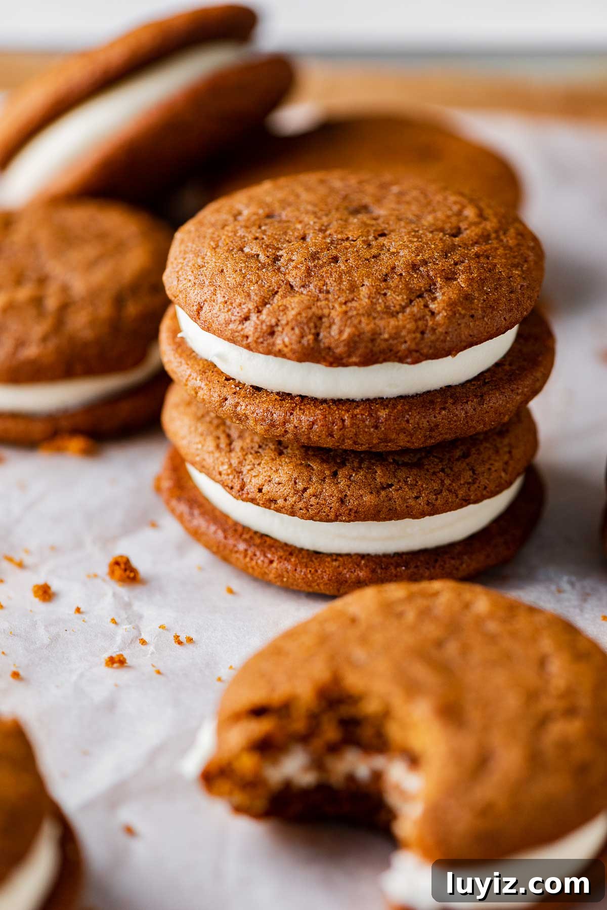 Gingerbread Whoopie Pies Recipe: Soft Molasses Sandwich Cookies 4 Stacked gingerbread whoopie pies filled with cream cheese frosting on a parchment paper lined baking sheet | © Beyond the Butter®