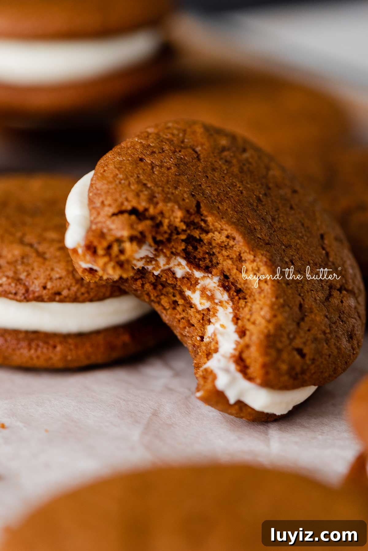 Gingerbread Whoopie Pies Recipe: Soft Molasses Sandwich Cookies 8 Half eaten homemade gingerbread whoopie pie stacked with more whoopie pies on parchment paper | © Beyond the Butter®