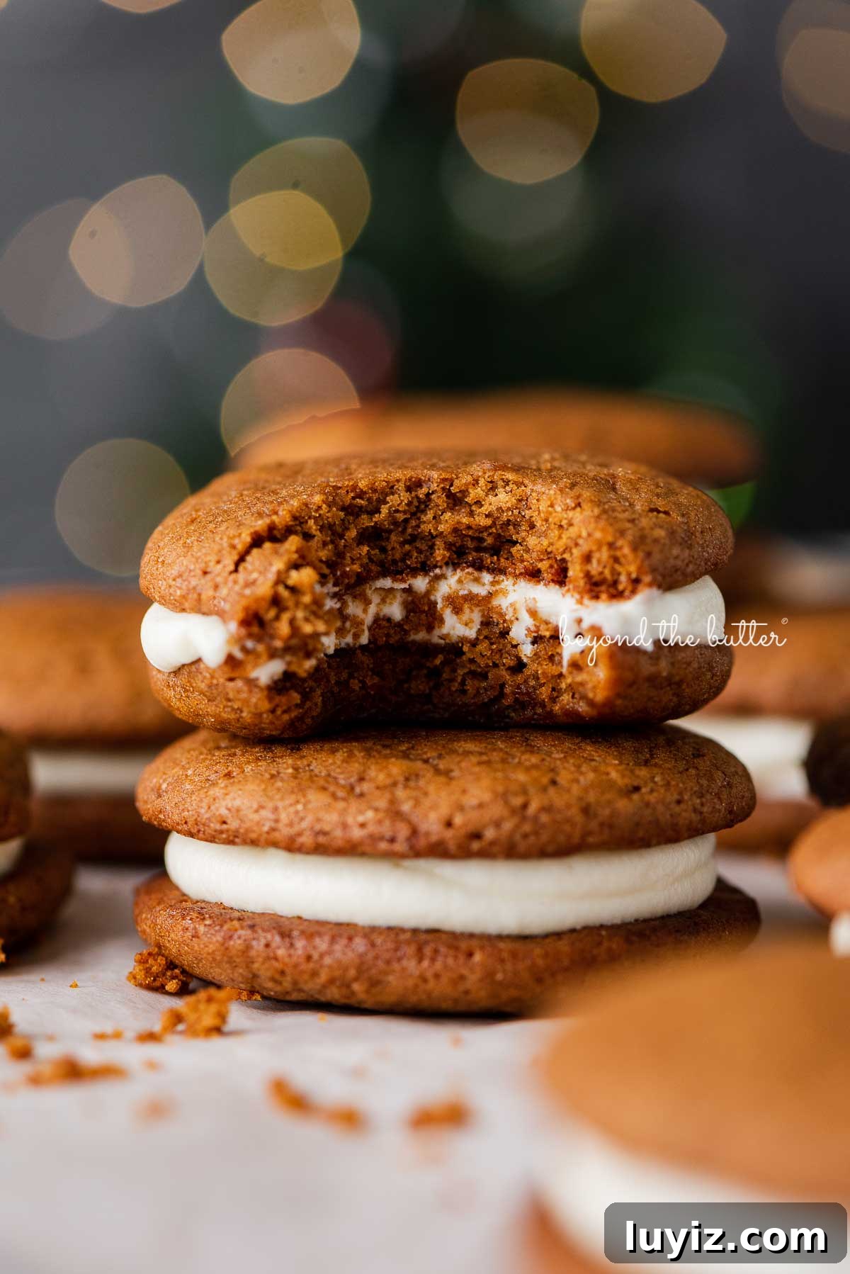 Gingerbread Whoopie Pies Recipe: Soft Molasses Sandwich Cookies 10 Half eaten gingerbread whoopie pie placed on top of another whoopie pie with a holiday tree background | © Beyond the Butter®