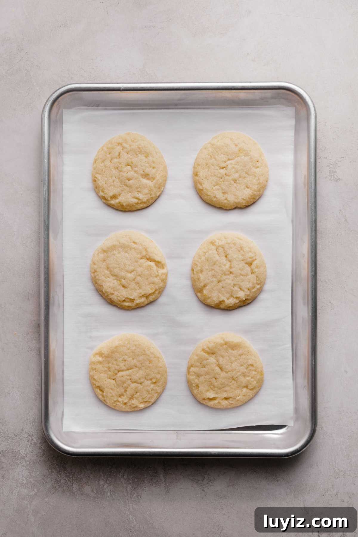 Zesty Lemon Shortbread Cookies: Crispy, Buttery Citrus Treats 11 Just baked lemon shortbread cookies on a white parchment paper lined baking sheet on a grey marbled background.