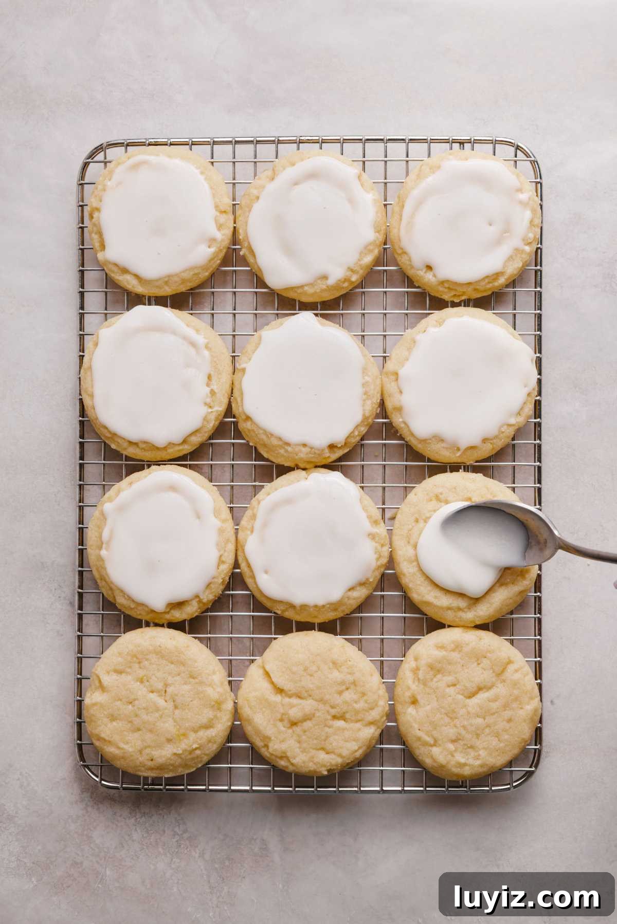 Zesty Lemon Shortbread Cookies: Crispy, Buttery Citrus Treats 13 Topping lemon shortbread cookies on a wire cooling rack with lemon glaze using a spoon.