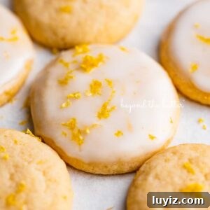Zesty Lemon Shortbread Cookies: Crispy, Buttery Citrus Treats 19 Lemon iced and plain lemon shortbread cookies garnished with lemon zest on white parchment paper.