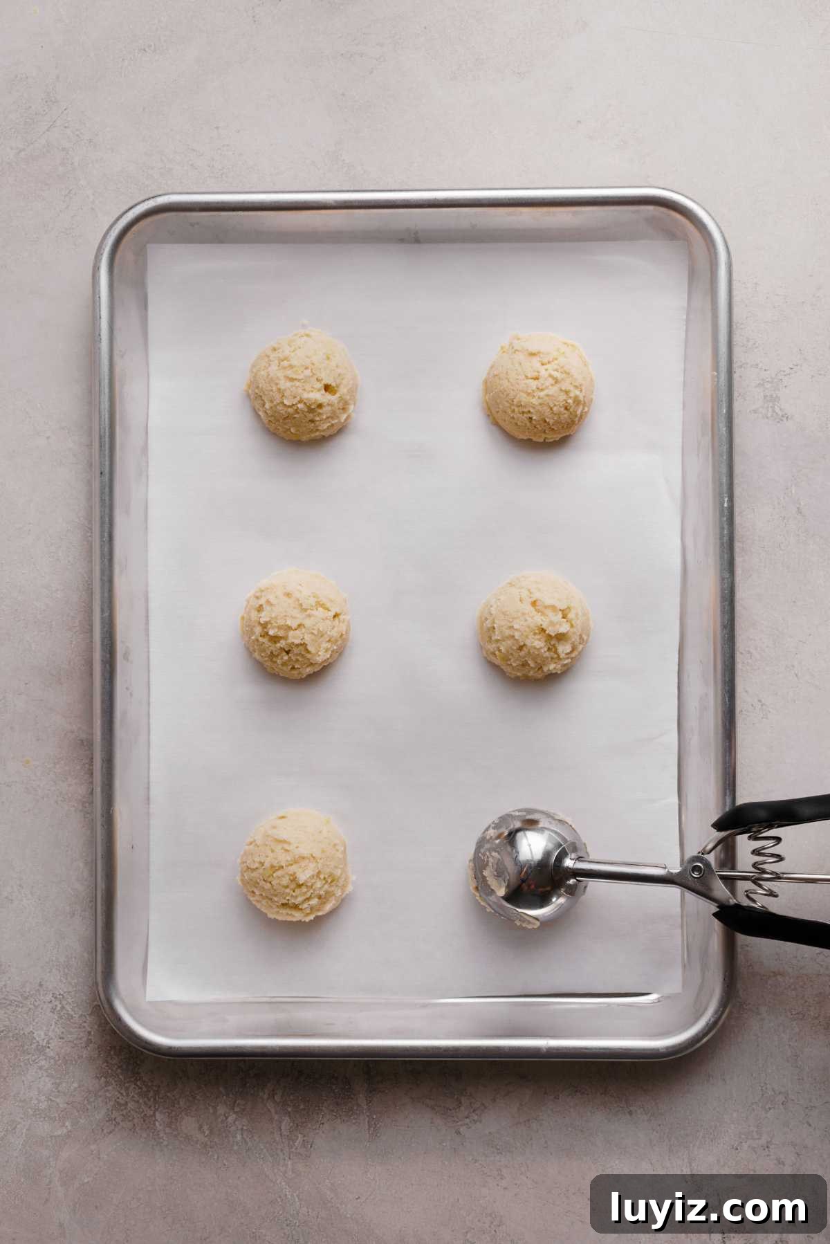 Zesty Lemon Shortbread Cookies: Crispy, Buttery Citrus Treats 9 Scoops of lemon shortbread cookie dough on a white parchment paper lined baking sheet using a cookie scoop.