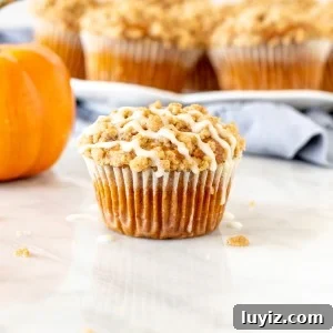 Pumpkin Streusel Muffins Recipe with Cinnamon Crunch Topping 8 Pumpkin streusel muffin with glaze on top, with a plate of muffins in the background.