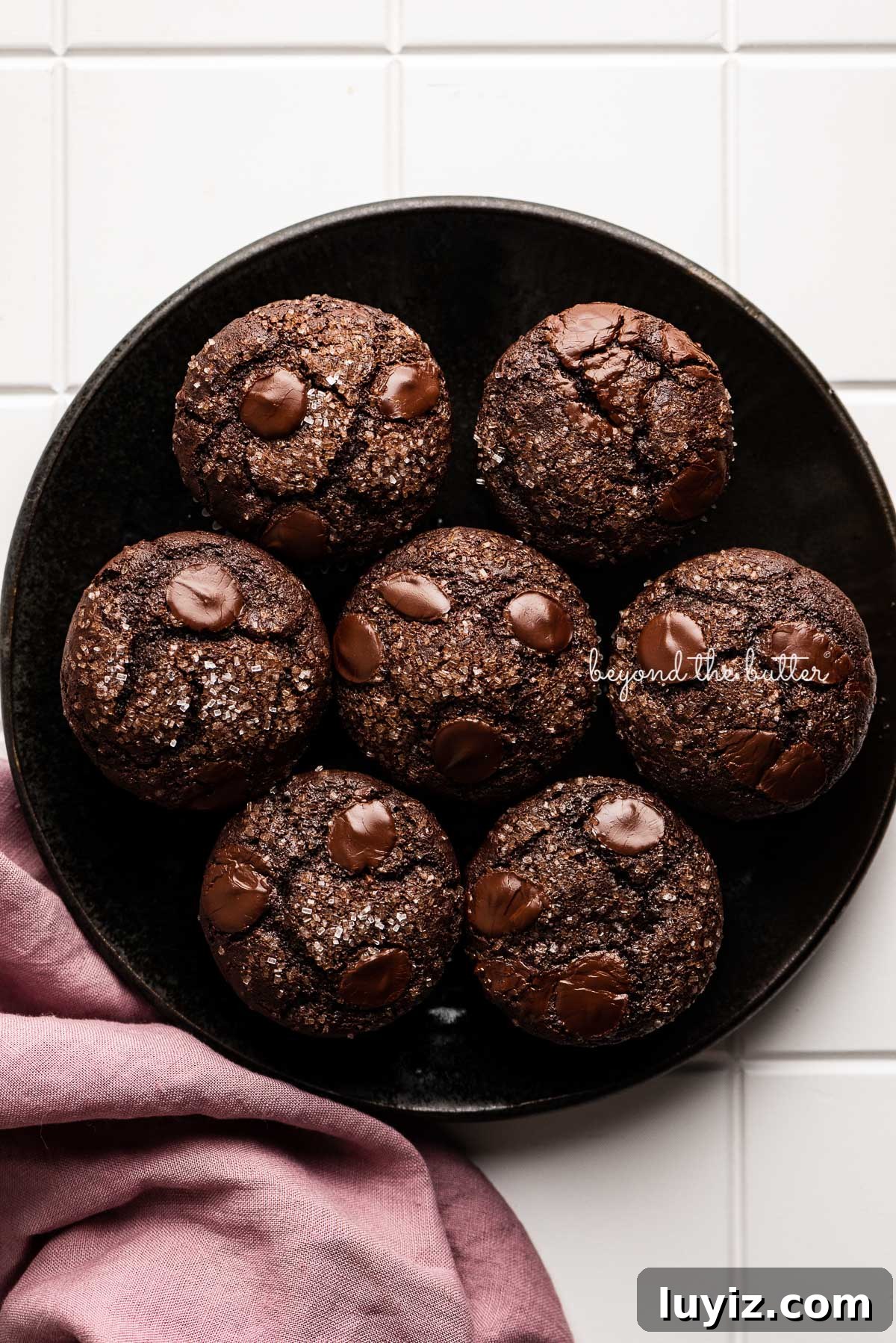 Ultimate Double Chocolate Muffins Recipe – Moist & Fudgy 10 Black ceramic dessert plate topped with double chocolate muffins with a mauve colored linen napking to the left | © Beyond the Butter®