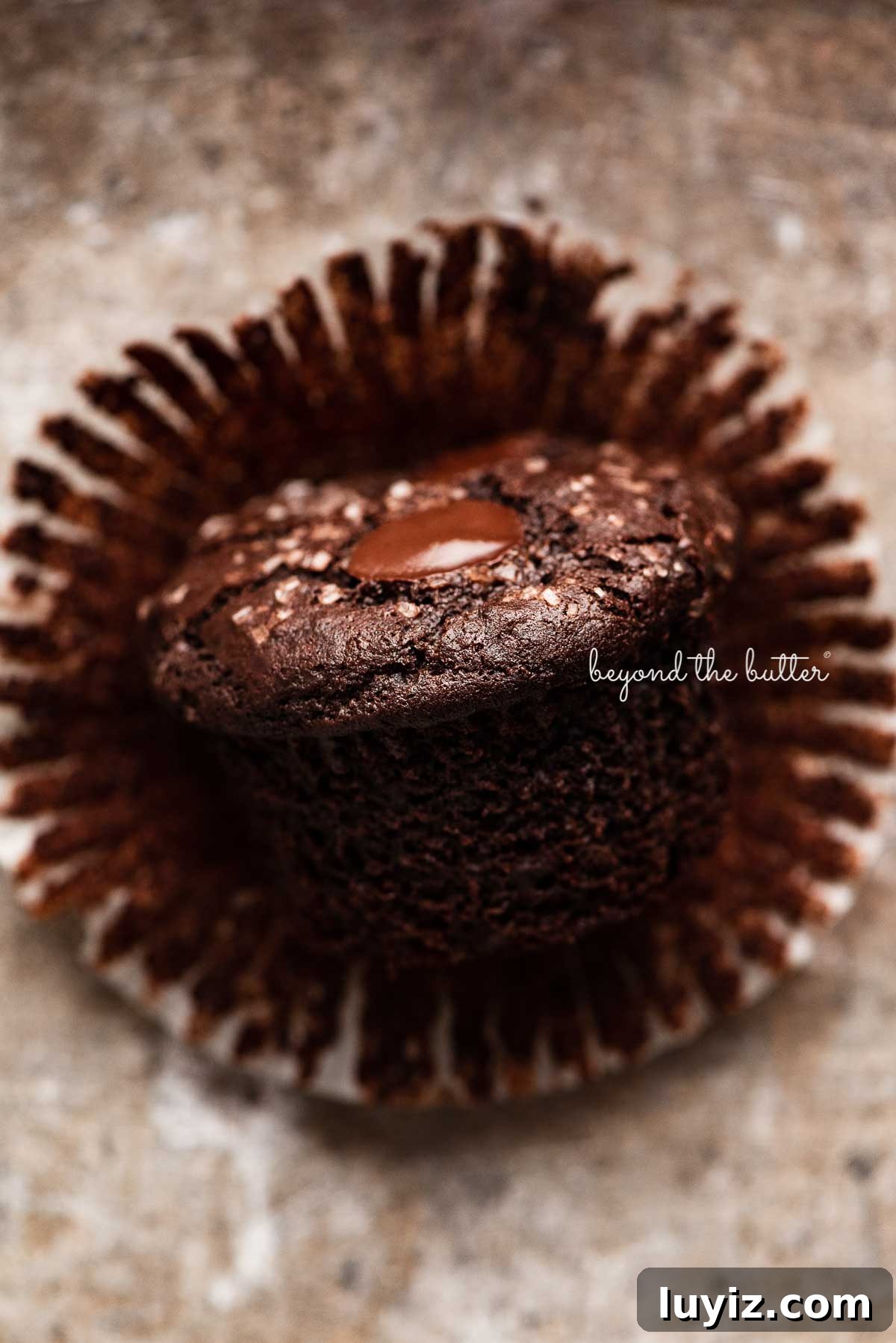 Ultimate Double Chocolate Muffins Recipe – Moist & Fudgy 6 One double chocolate chip muffin without the liner on it's side on light vintage gray background | © Beyond the Butter®