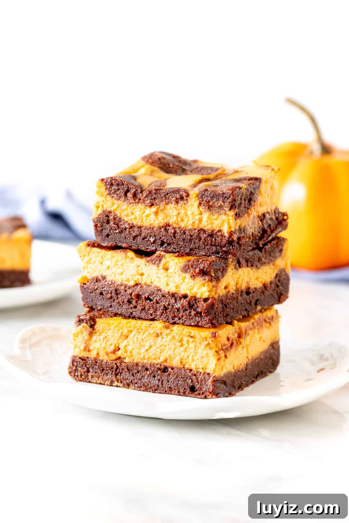 Pumpkin Cheesecake Brownies Recipe — Creamy Swirl Dessert 2 3 pumpkin cheesecake brownies stacked on top of each other.