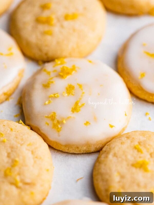 Moist Lemon Cream Cheese Pound Cake Recipe 11 Lemon iced and plain lemon shortbread cookies garnished with lemon zest on white parchment paper.