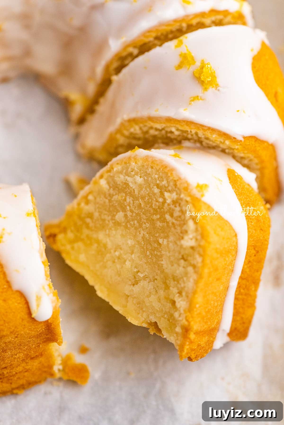 Moist Lemon Cream Cheese Pound Cake Recipe 7 Sliced lemon cream cheese pound cake on white parchment paper | © Beyond the Butter®
