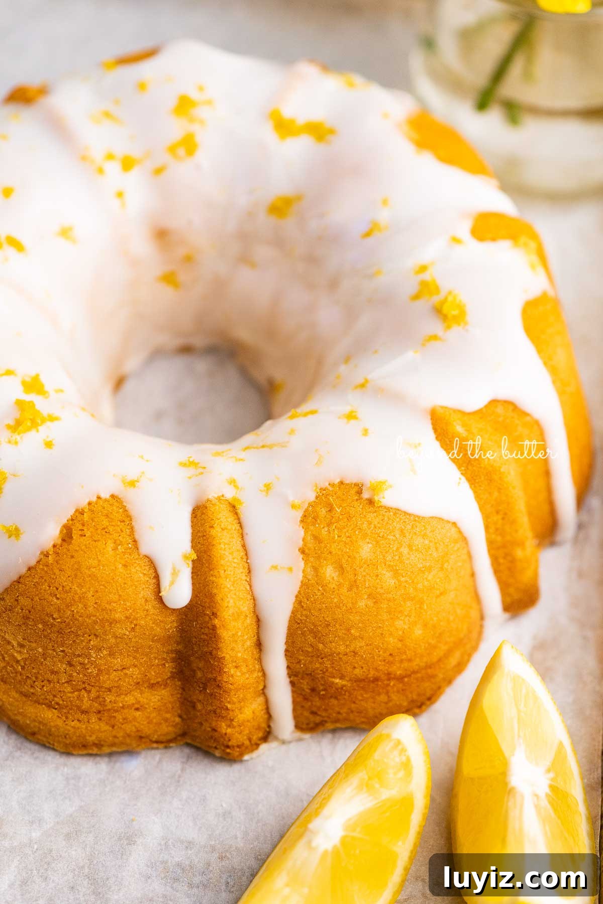 Moist Lemon Cream Cheese Pound Cake Recipe 8 Small lemon cream cheese pound cake topped with a simple lemon glaze on a parchment paper lined baking sheet with sliced lemons | © Beyond the Butter®