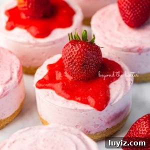 Mini No-Bake Strawberry Cheesecakes (Individual Cups) 13 Individual no-bake strawberry cheesecakes topped with strawberry glaze and a fresh strawberry on a parchment paper-lined baking sheet.