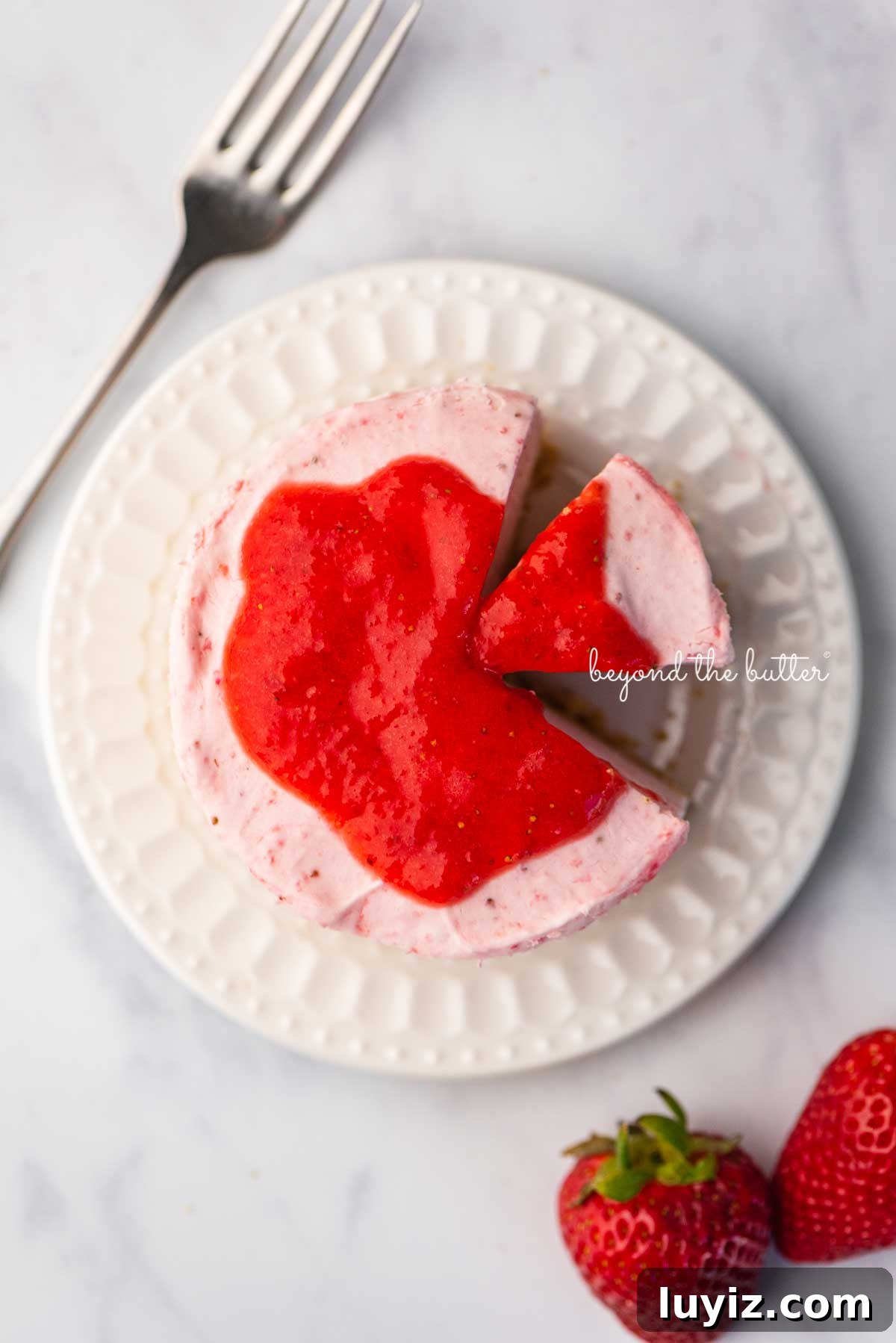 Mini No-Bake Strawberry Cheesecakes (Individual Cups) 4 Small 4-inch no-bake strawberry cheesecake on a white dessert plate with a fork and fresh strawberries nearby on a marbled background | © Beyond the Butter®
