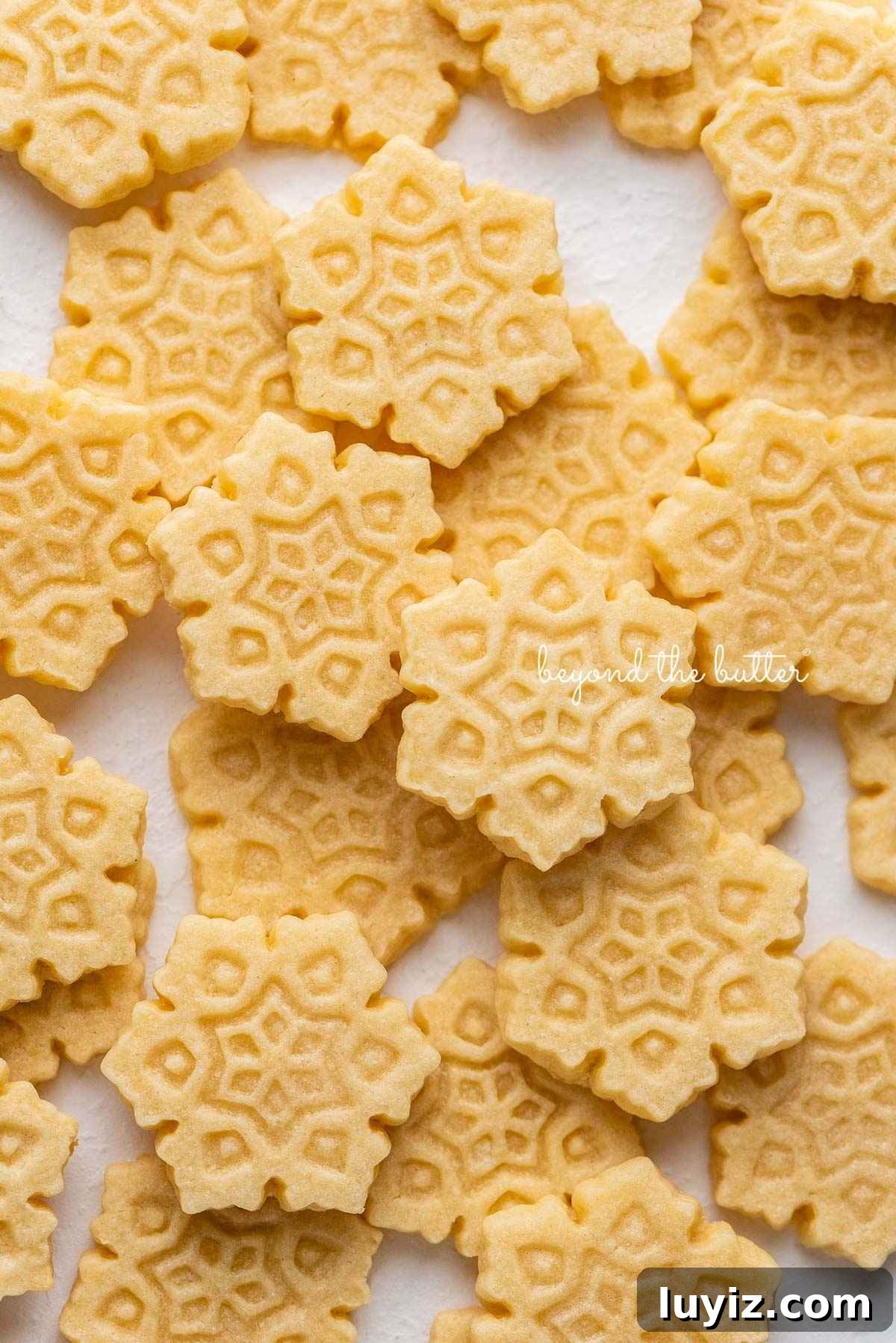 Classic Homemade Butter Cookies Recipe — Crisp, Melt-in-Your-Mouth Cookies 2 Butter cookies shaped as snowflakes randomly placed on a white parchment paper lined baking sheet.