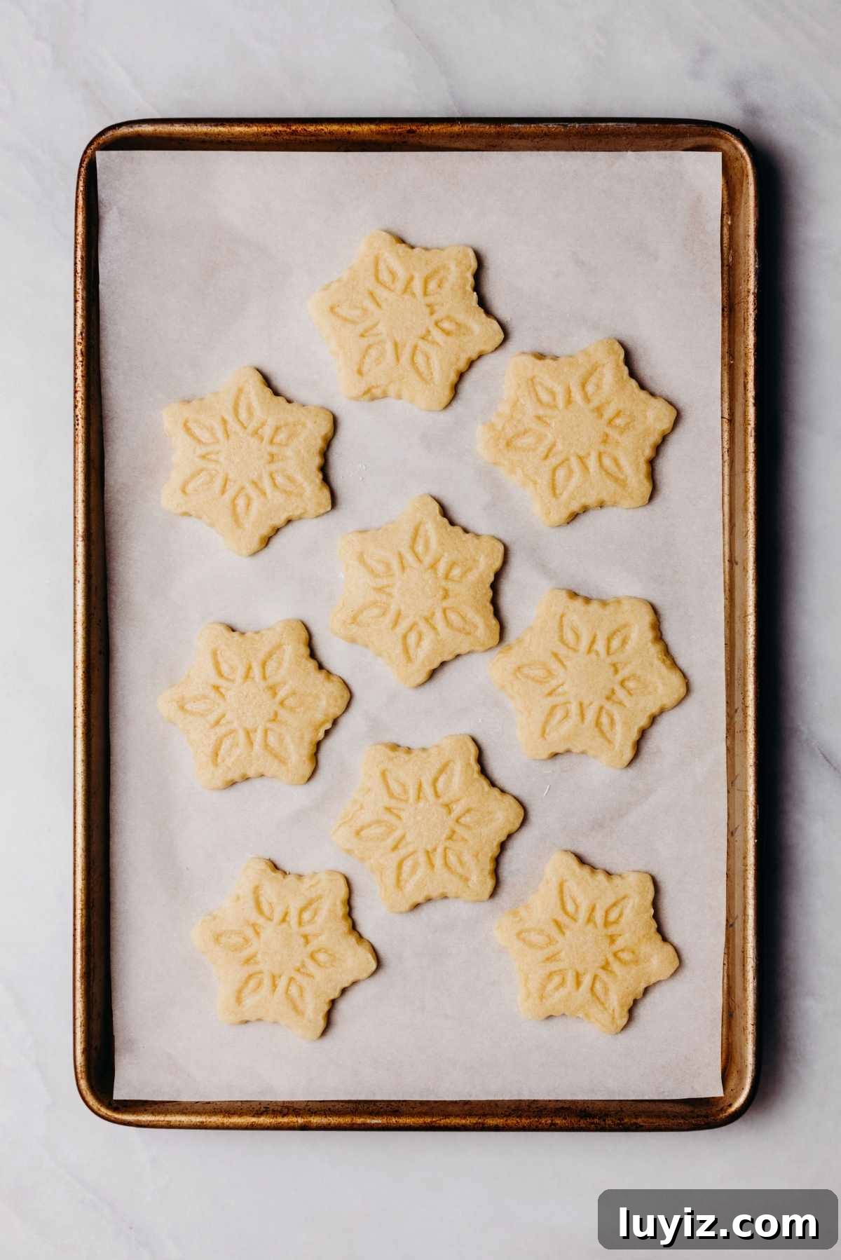 Classic Homemade Butter Cookies Recipe — Crisp, Melt-in-Your-Mouth Cookies 12 Baked homemade butter cookies on a white parchment paper lined baking sheet on a white and grey marbled background.