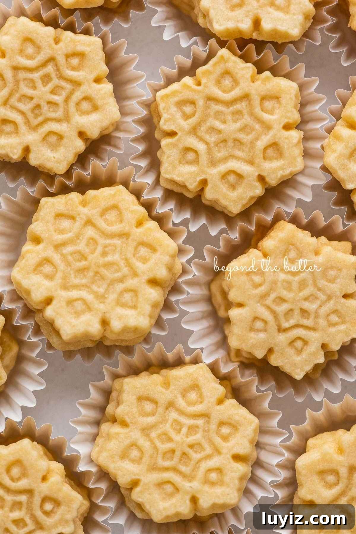 Classic Homemade Butter Cookies Recipe — Crisp, Melt-in-Your-Mouth Cookies 14 Stacks of homemade butter cookies shaped like snowflakes in white cupcake liners.