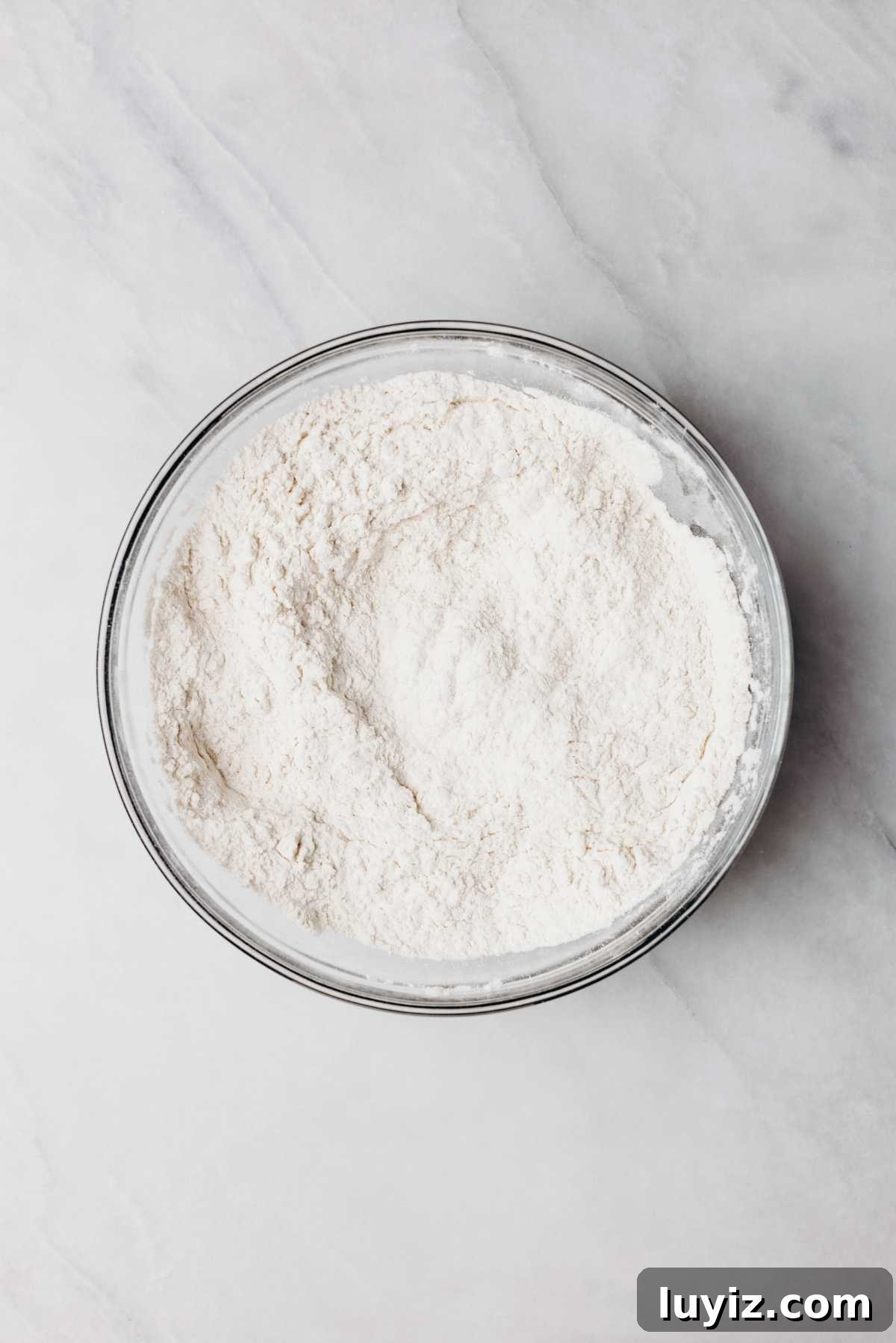 Classic Homemade Butter Cookies Recipe — Crisp, Melt-in-Your-Mouth Cookies 6 Whisked all purpose flour, baking powder, and salt in a glass mixing bowl on a white and grey marbled background.