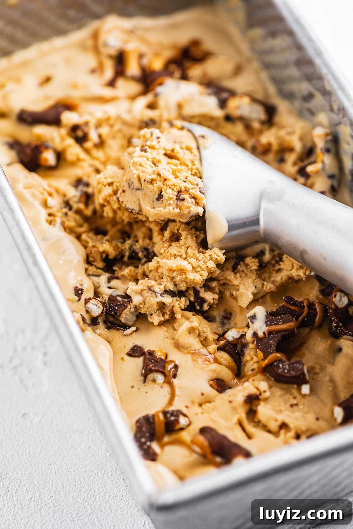 Dulce de Leche Ice Cream with Chocolate-Covered Pretzels 5 Ice cream scoop in a container of dulce de leche ice cream with chocolate covered pretzels