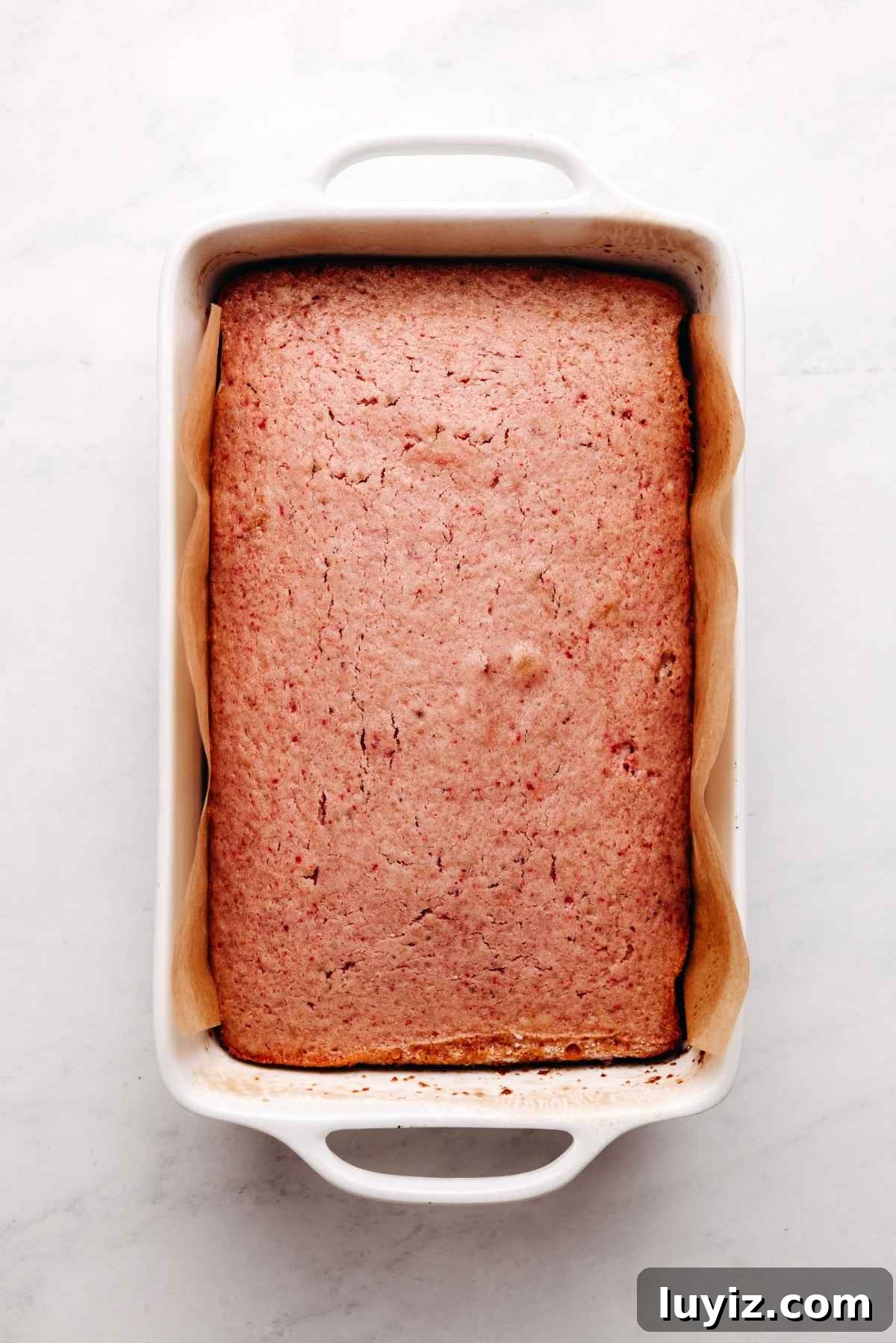 Mini Strawberry Sheet Cake Recipe: Quick Moist Fresh Strawberry Cake 15 Baked mini strawberry sheet cake in a parchment paper lined baking tin on a white and grey textured background.