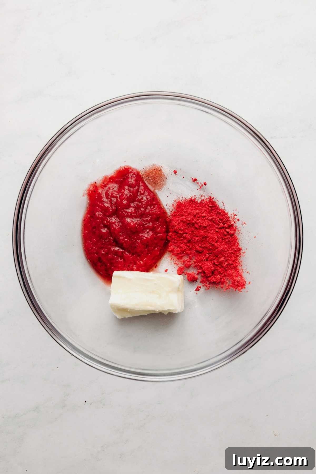 Mini Strawberry Sheet Cake Recipe: Quick Moist Fresh Strawberry Cake 16 Strawberry puree, freeze dried strawberry powder, butter, and salt in large glass mixing bowl on a white and grey textured background.