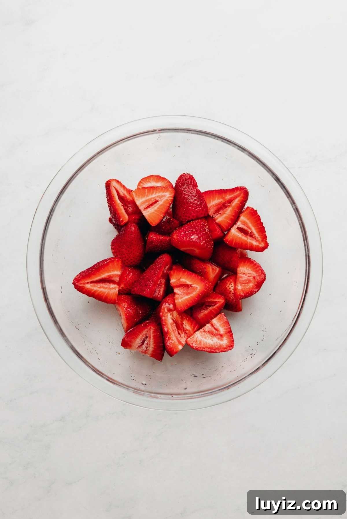 Mini Strawberry Sheet Cake Recipe: Quick Moist Fresh Strawberry Cake 6 Sliced strawberries, lemon juice, and granulated sugar tossed together in a small glass bowl on a white and grey textured background.