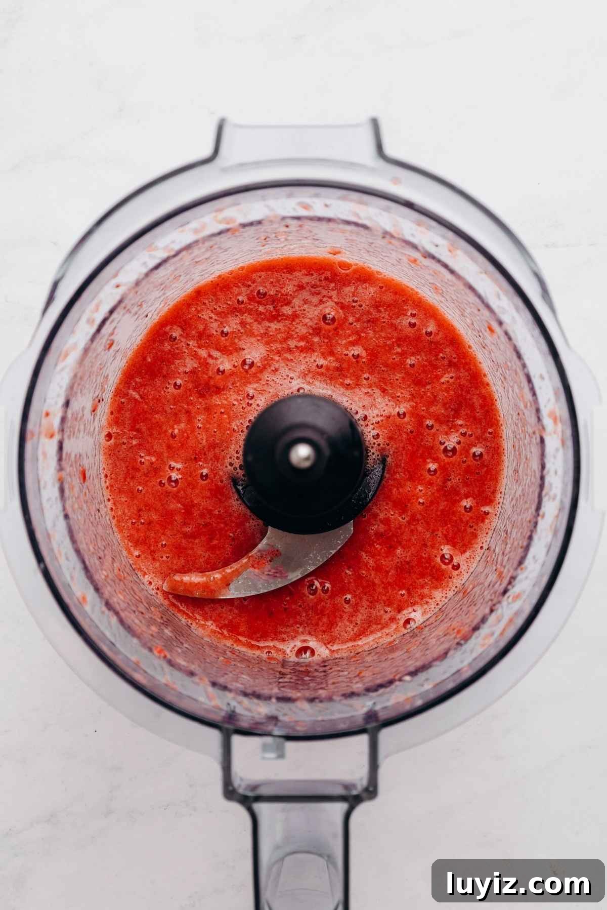 Mini Strawberry Sheet Cake Recipe: Quick Moist Fresh Strawberry Cake 9 Roasted strawberry puree in a food processor on a white and grey textured background.