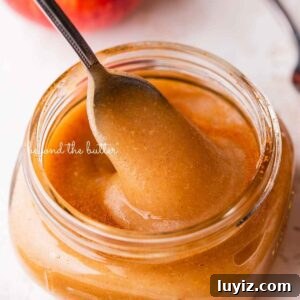 Homemade Applesauce Without Added Sugar: Simple Recipe 16 Filled glass jar of homemade applesauce with a spoon on white background with apples.