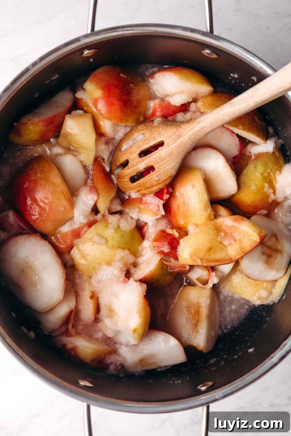 Homemade Applesauce Without Added Sugar: Simple Recipe 7 Stirring cooked and softened cortland apples in stockpot with a slotted wooden spoon.