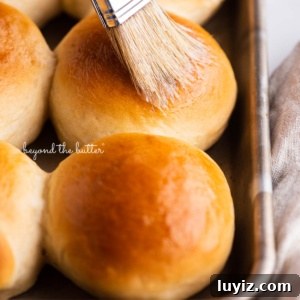 Soft Honey Butter Dinner Rolls Recipe for Fluffy, Golden Buns 8 Small tray of honey butter dinner rolls being brushed with more honey butter.
