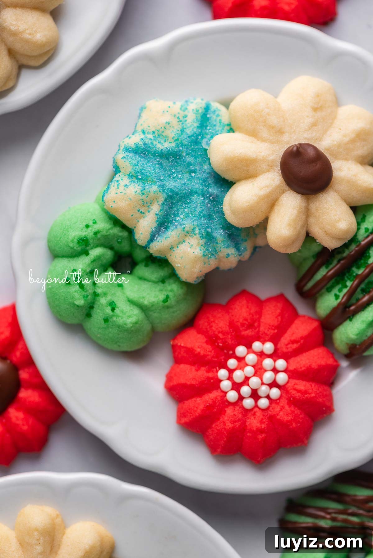 Crisp Butter Spritz Cookies: Traditional Holiday Recipe 3 Tiny dessert plates with classic spritz cookies on a white marble background | © Beyond the Butter®