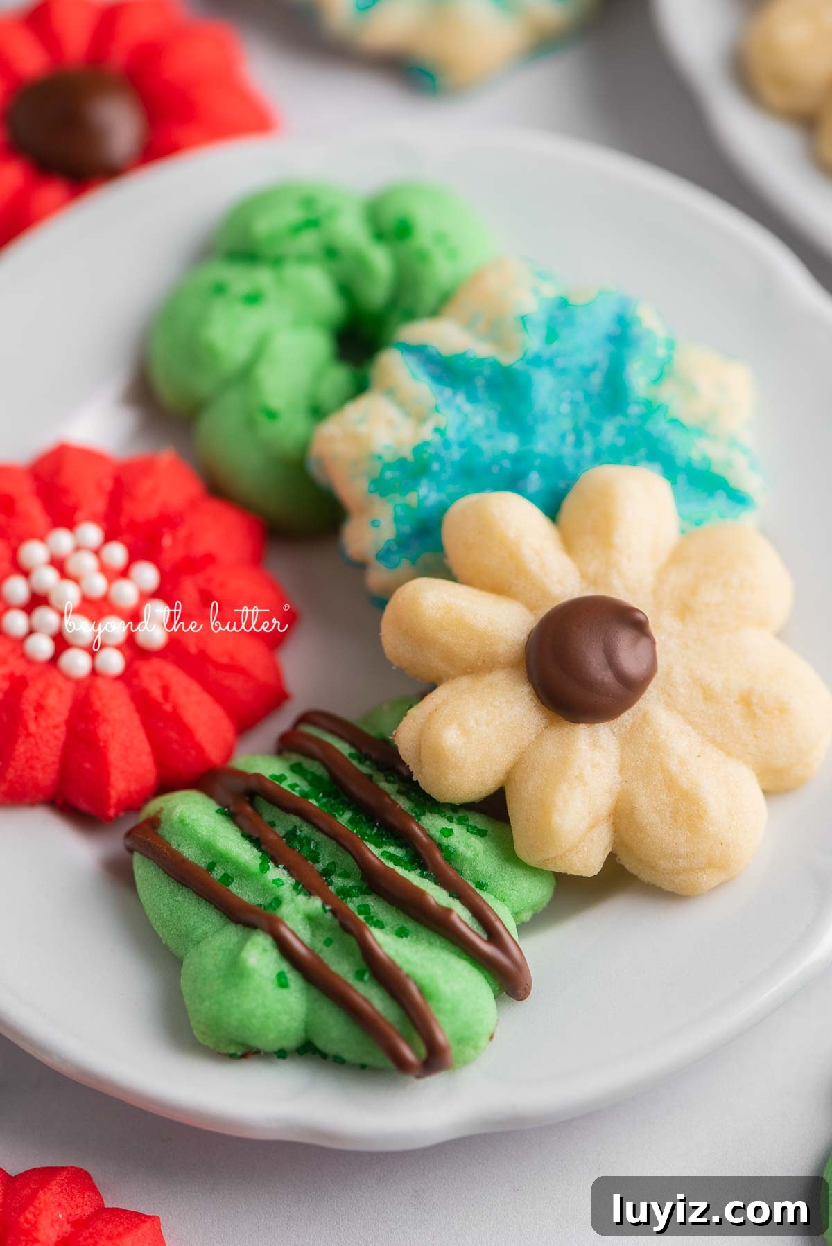 Crisp Butter Spritz Cookies: Traditional Holiday Recipe 6 Tiny dessert plates with classic spritz cookies on a white marble background | © Beyond the Butter®