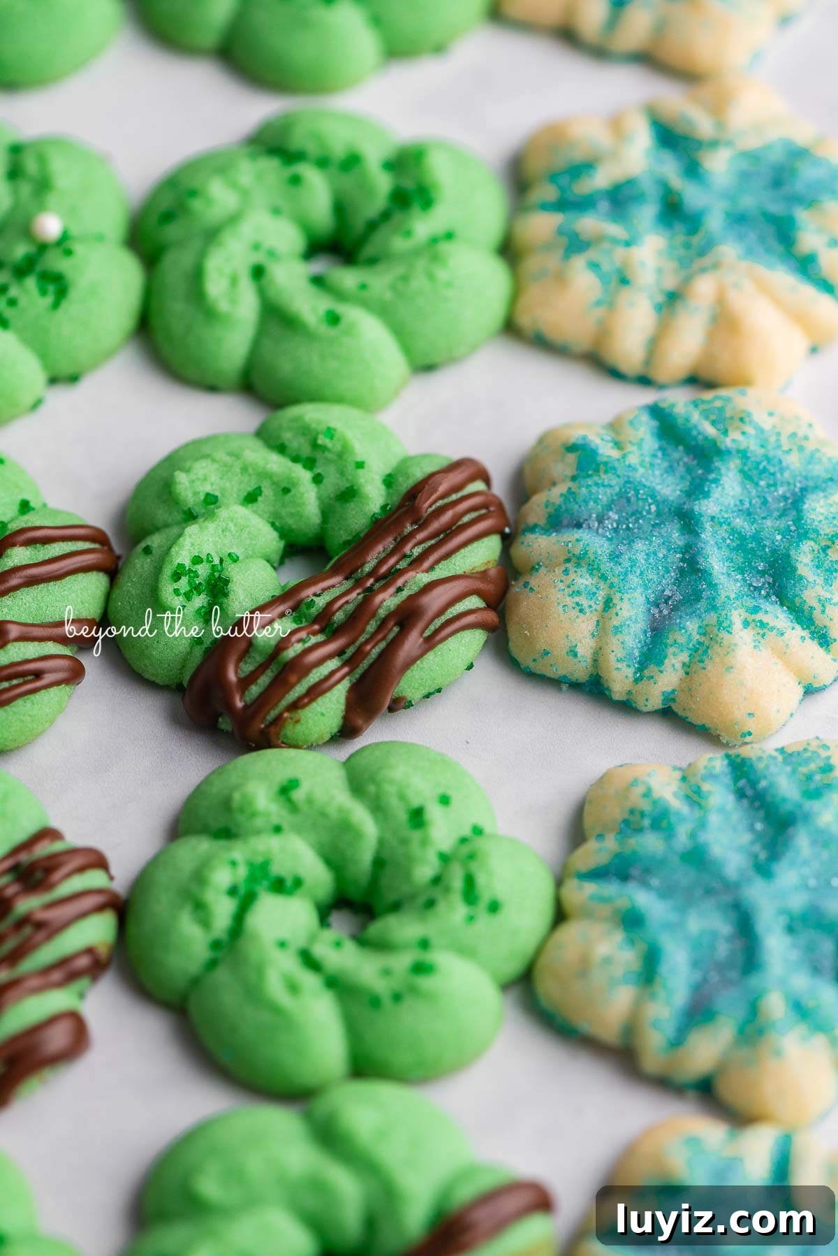 Crisp Butter Spritz Cookies: Traditional Holiday Recipe 7 Decorated classic buttery spritz cookies lined up on a white marbled background | © Beyond theButter®