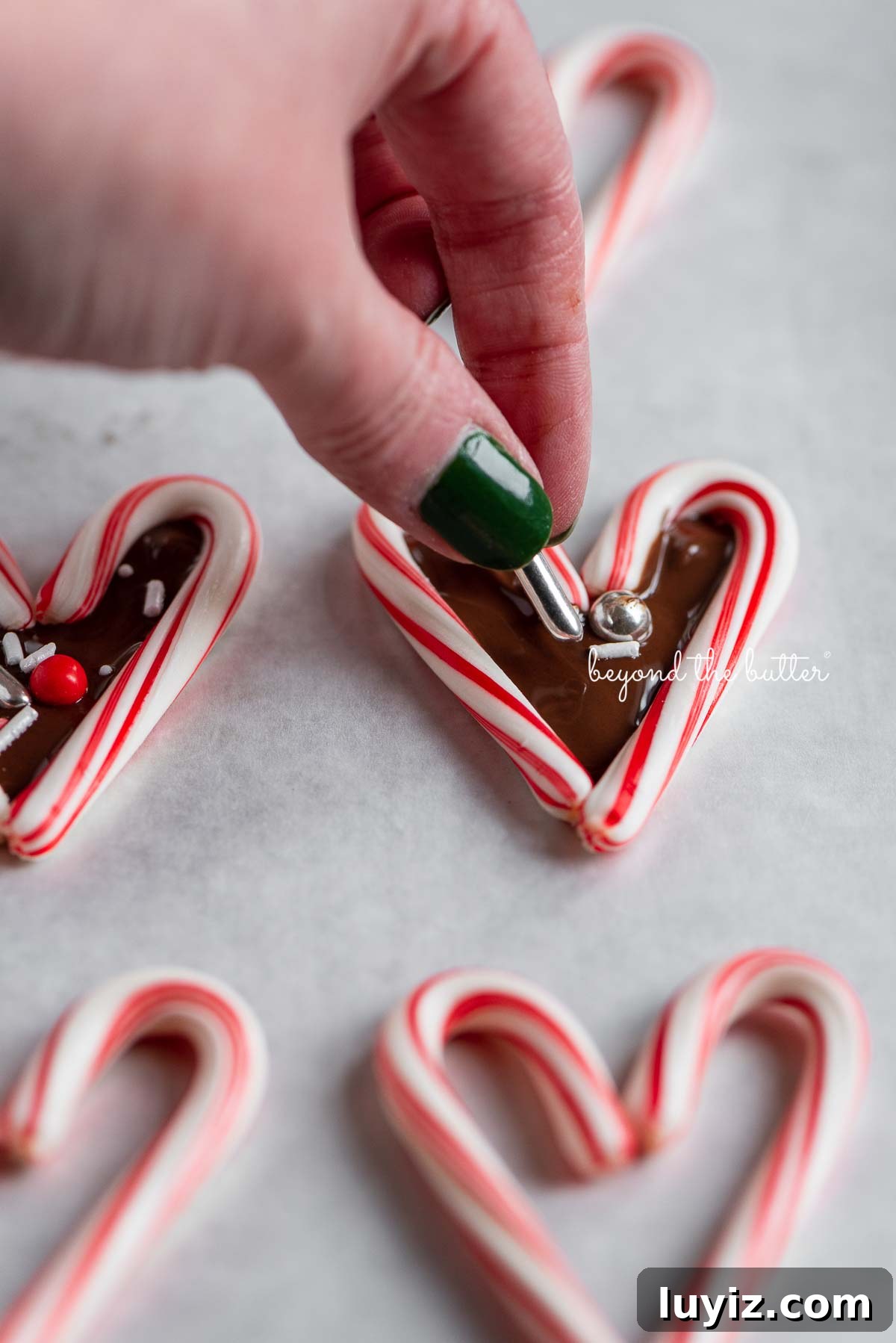 Candy Cane Heart Cookies: Festive Holiday Treats & Gift Ideas 5 Adding holiday theme sprinkles to candy cane hearts filled with melted chocolate | © Beyond the Butter®