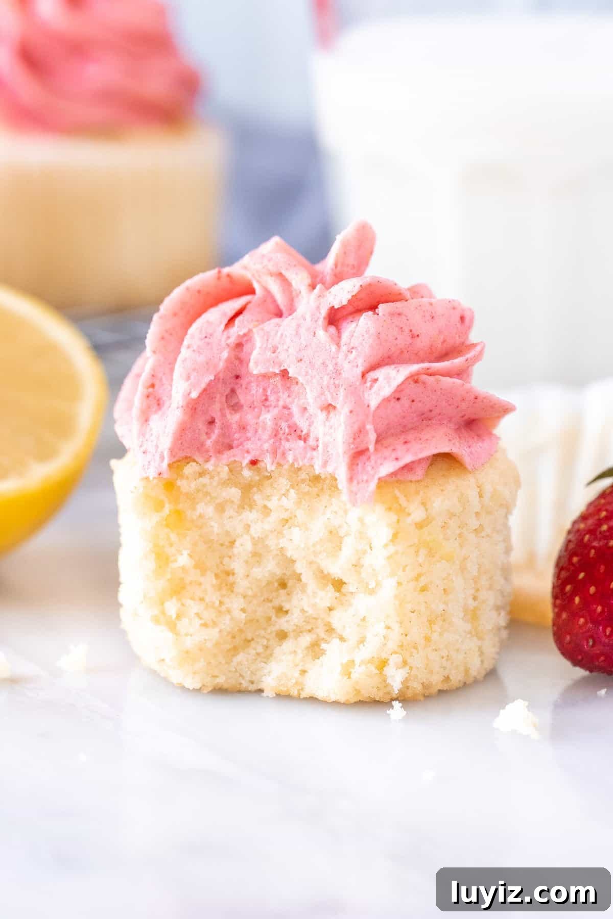 Strawberry Lemonade Cupcakes Recipe with Zesty Lemon Frosting 4 Strawberry lemonade cupcake with a bite taken out with a glass of milk