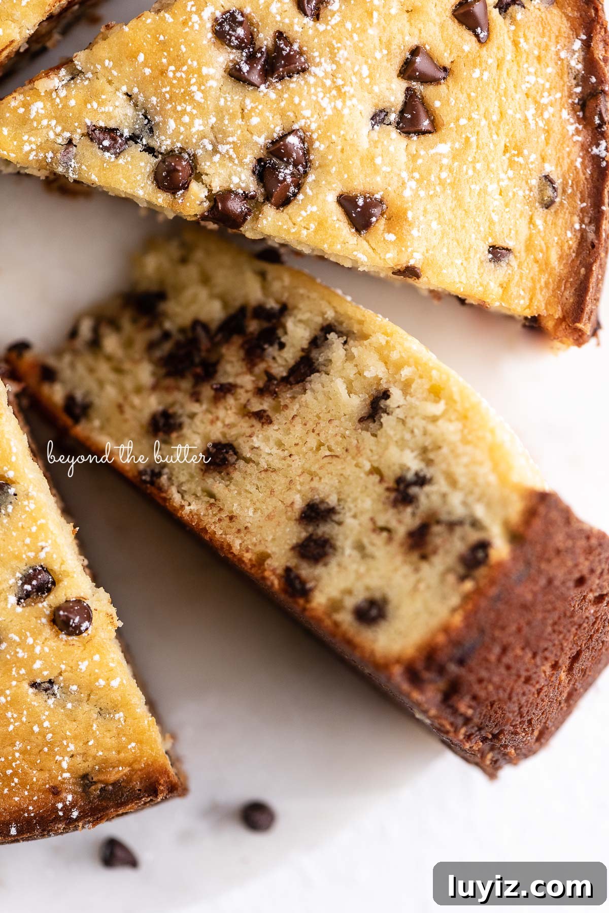 Moist Chocolate Chip Ricotta Cake Recipe for Perfect Dessert 4 Slices of chocolate chip ricotta cake with one on its side on a marble cake round with small bowl of mini chocolate chips nearby | © Beyond the Butter®