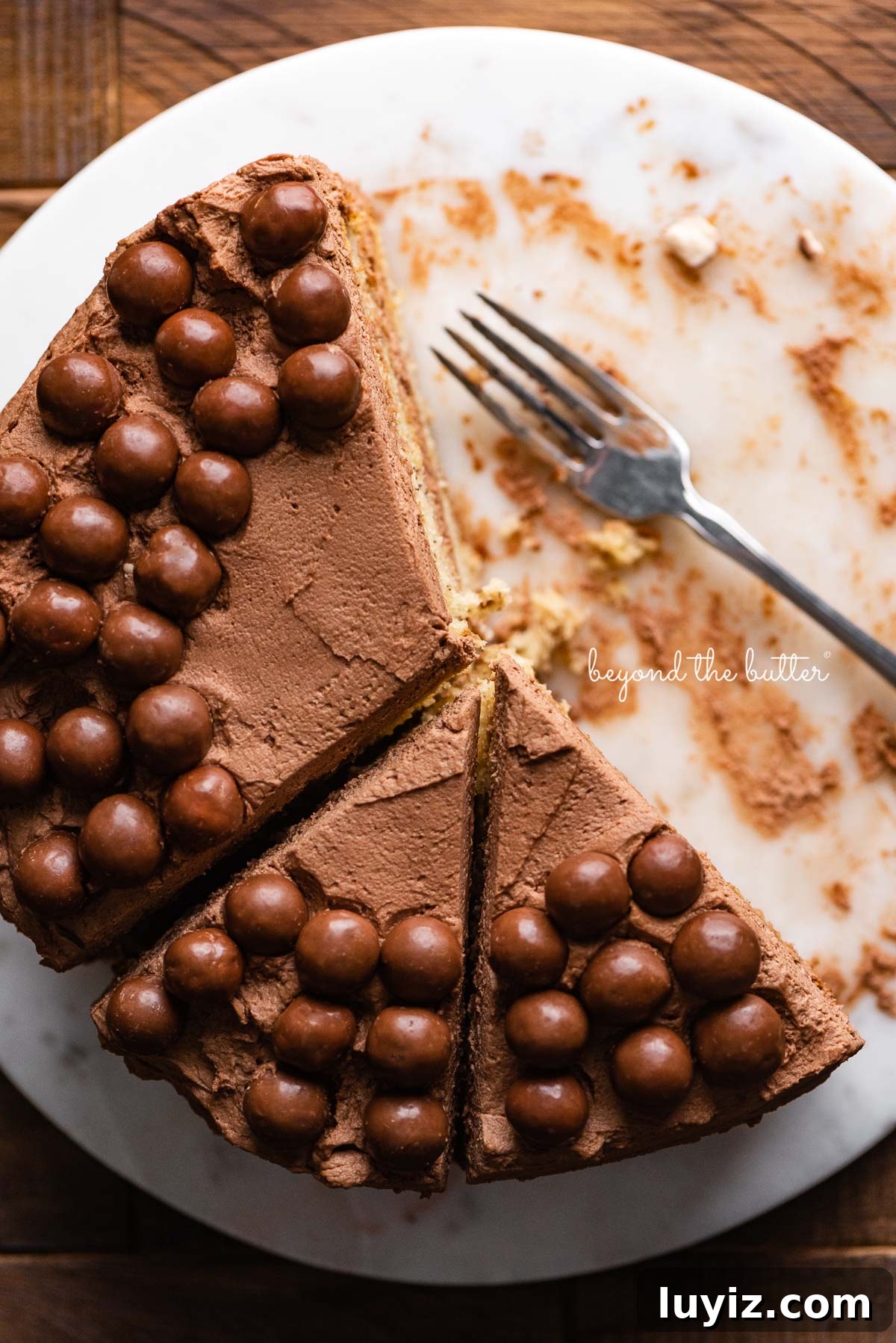 Ultra-Moist Banana Cake Recipe with Cream Cheese Frosting 4 Top down view of banana cake frosted with malted chocolate mascarpone whipped cream and garnished with malted chocolate balls on marble cake board | © Beyond the Butter®
