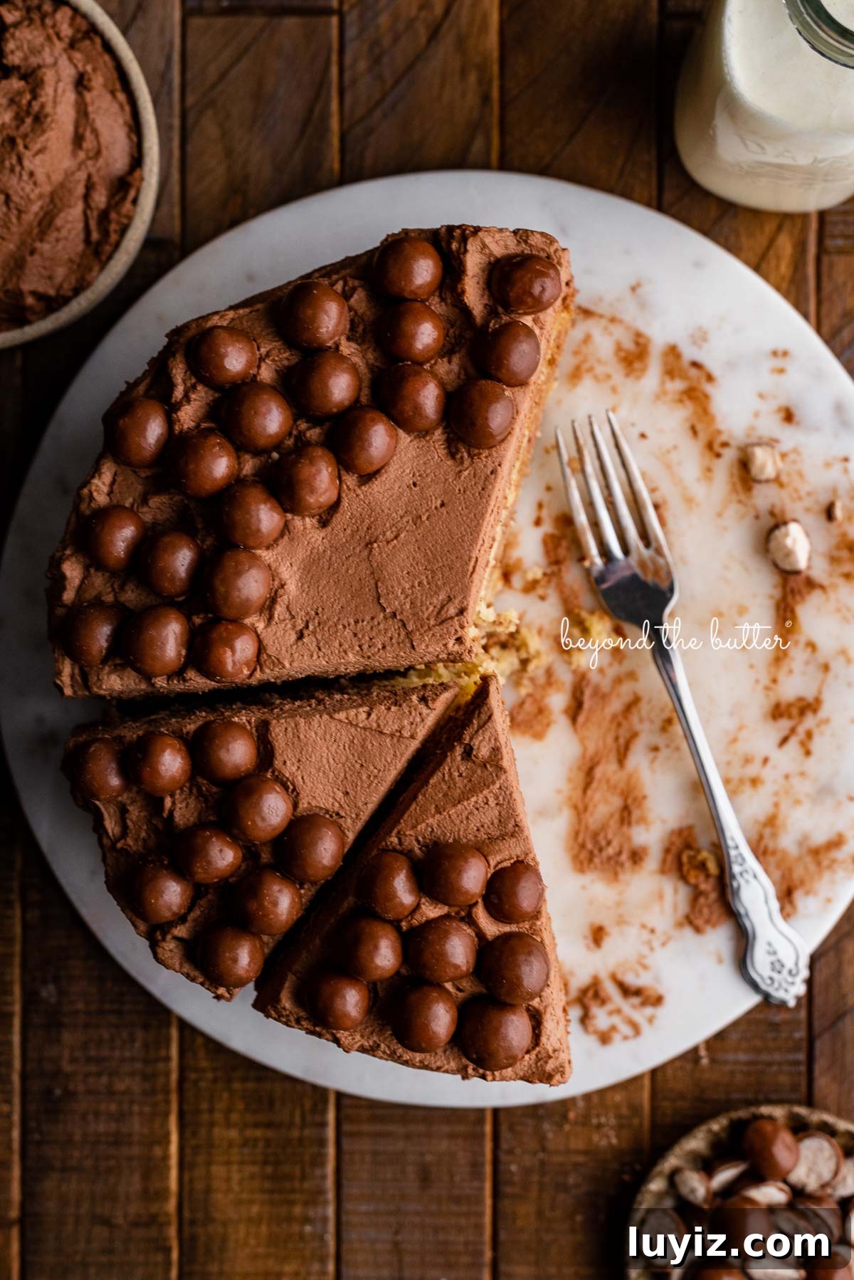 Ultra-Moist Banana Cake Recipe with Cream Cheese Frosting 5 Top down view of 2 layer moist banana cake frosted with malted chocolate mascarpone whipped cream and garnished with malted chocolate balls on marble cake board | © Beyond the Butter®