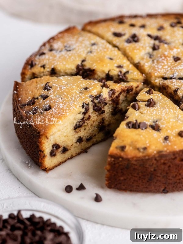 Ultra-Moist Banana Cake Recipe with Cream Cheese Frosting 6 Slices of chocolate chip ricotta cake on a marble cake round with small bowl of mini chocolate chips nearby.