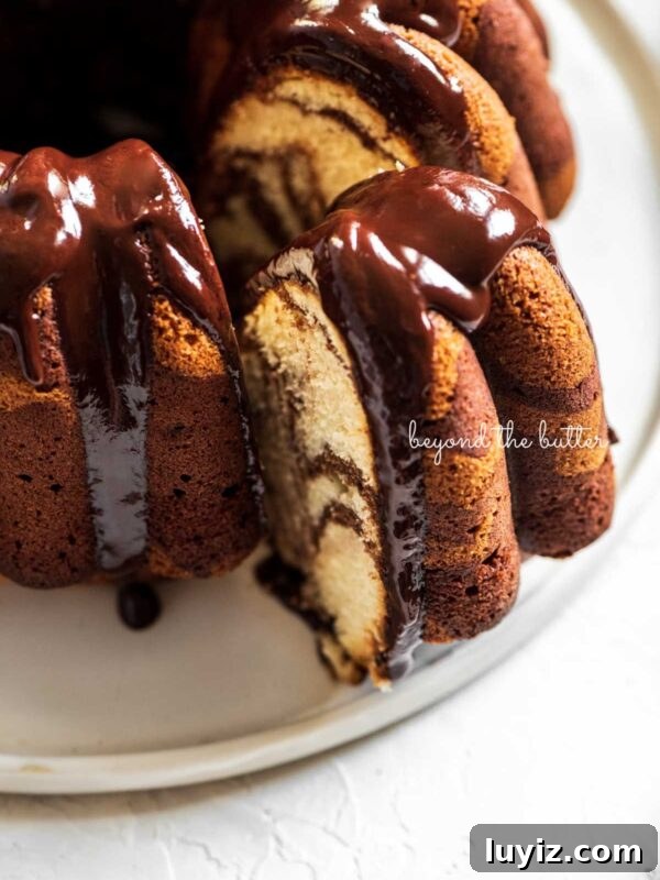 Ultra-Moist Banana Cake Recipe with Cream Cheese Frosting 9 Chocolate glazed marble bundt cake with one slice partially removed on a white ceramic dessert plate and white background.