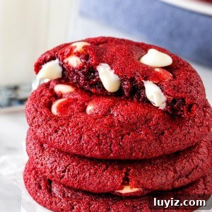 A stack of red velvet chocolate chip cookies, with the top cookie broken in half.