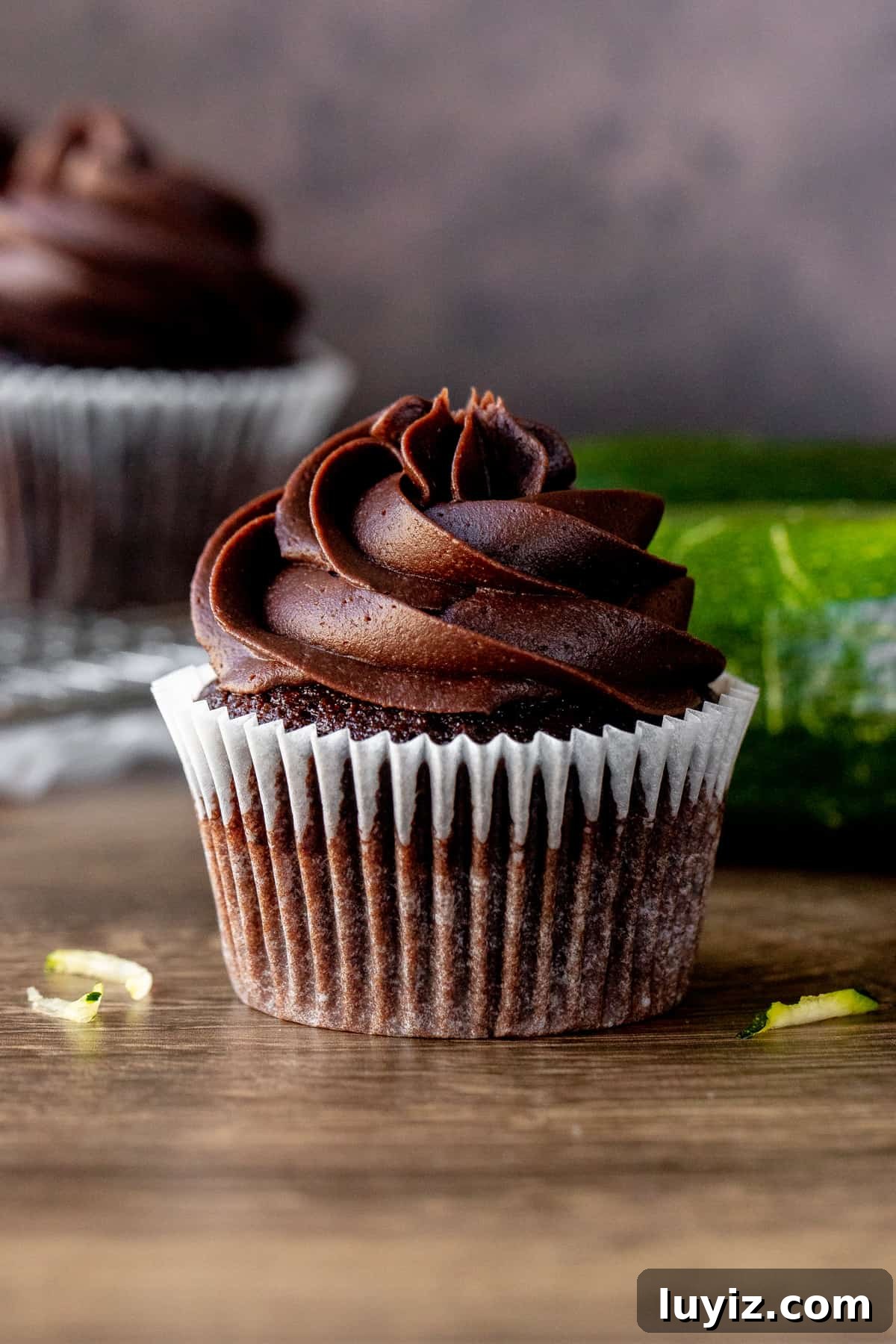 Decadent Chocolate Zucchini Cupcakes with Moist Fudgy Texture 2 Chocolate zucchini cupcake with zucchini and cupcakes in background