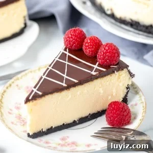 Piece of white chocolate cheesecake, topped with chocolate ganache & decorated with raspberries