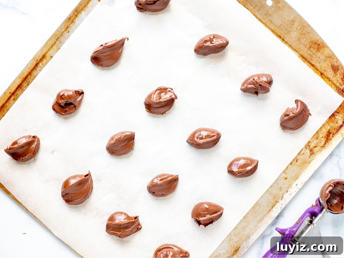 Decadent Nutella-Filled Chocolate Chip Cookies 3 Spoonfuls of Nutella on a lined cookie sheet